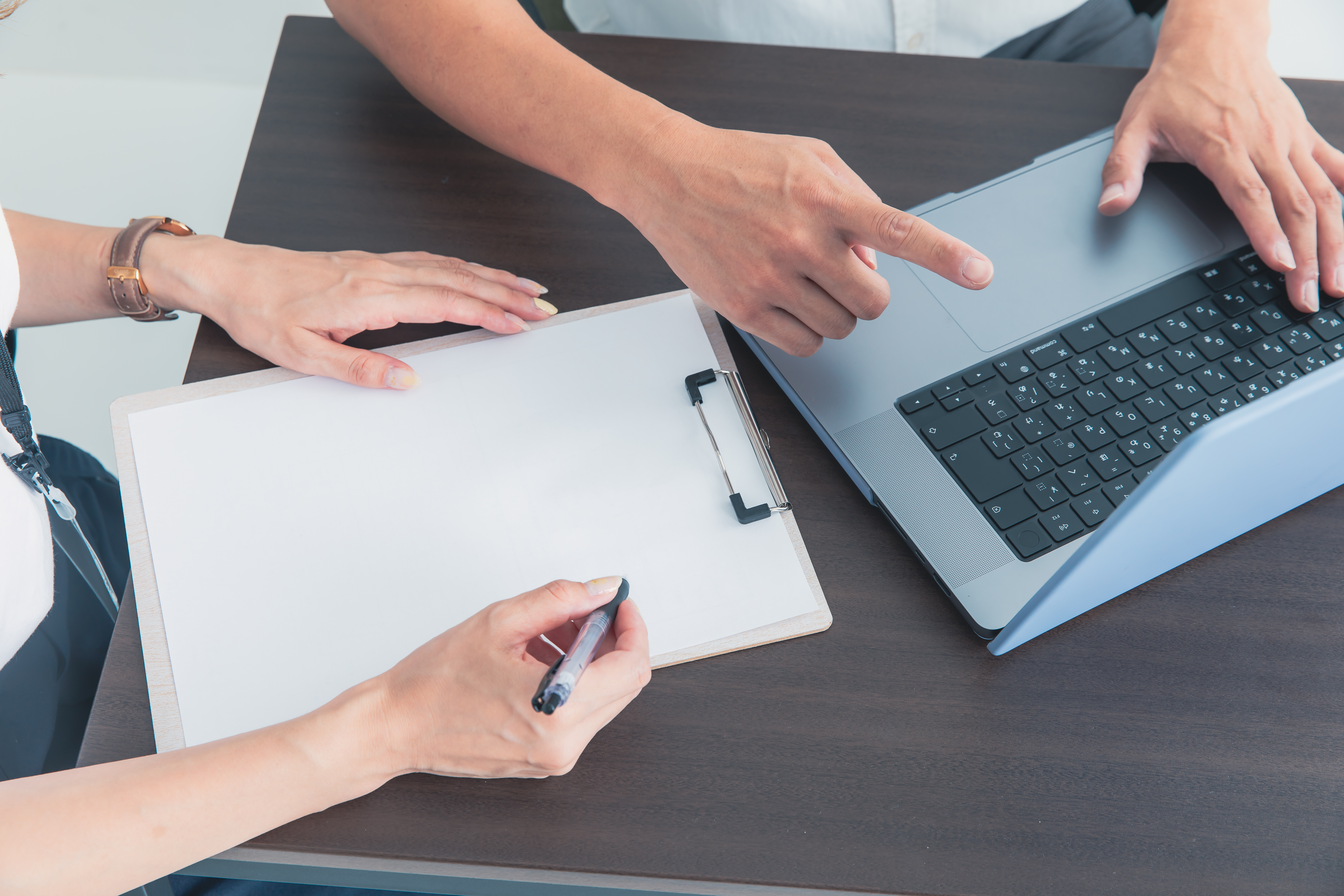 インハウスSEOの実務作業。PCでキーワード調査を行いながら、施策内容を書類にまとめる担当者の手元。