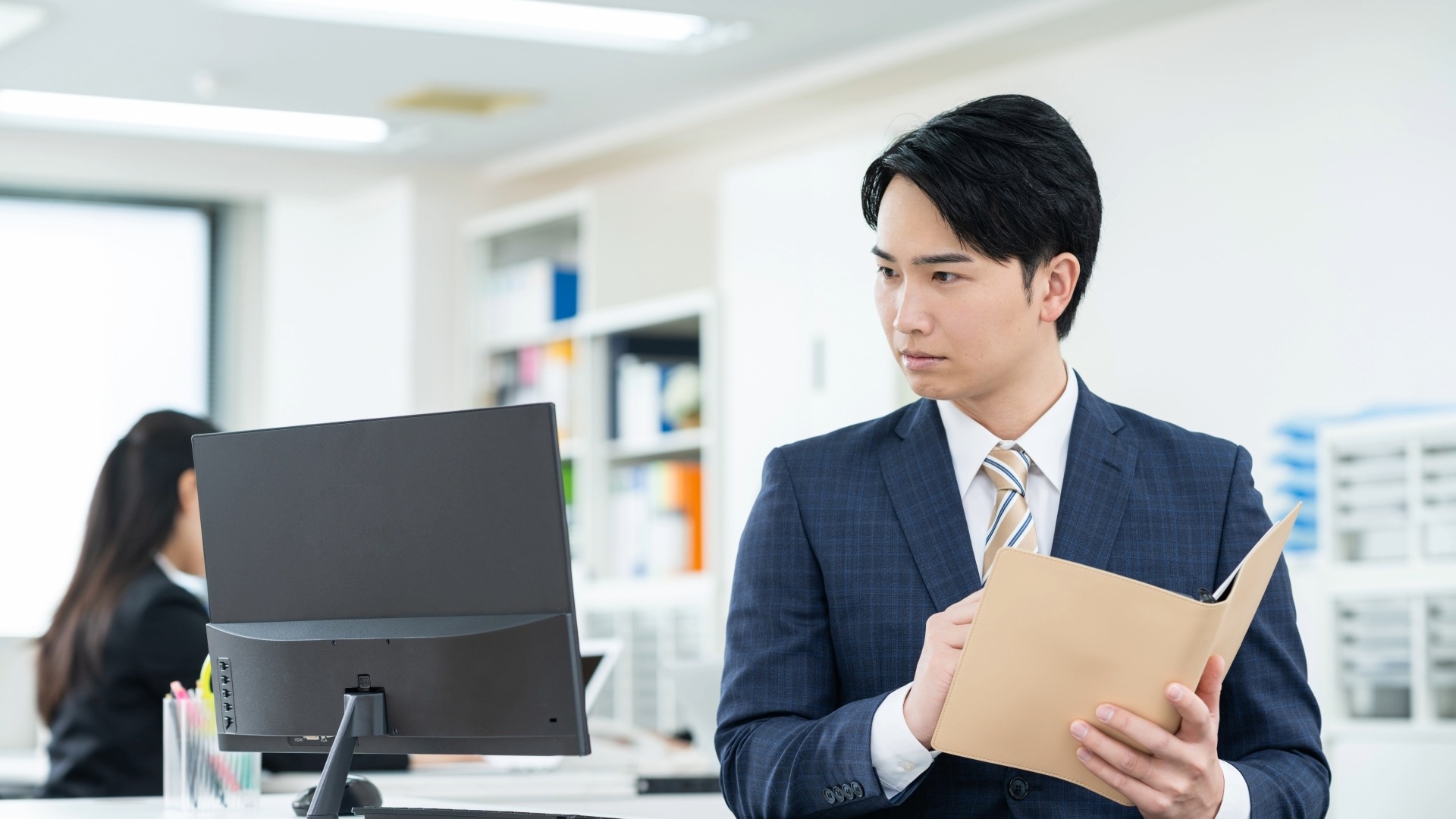 オウンドメディアのKPI設計に向けて、PCで現状の数値を分析しながら改善策を手帳に書き出すビジネスマン。