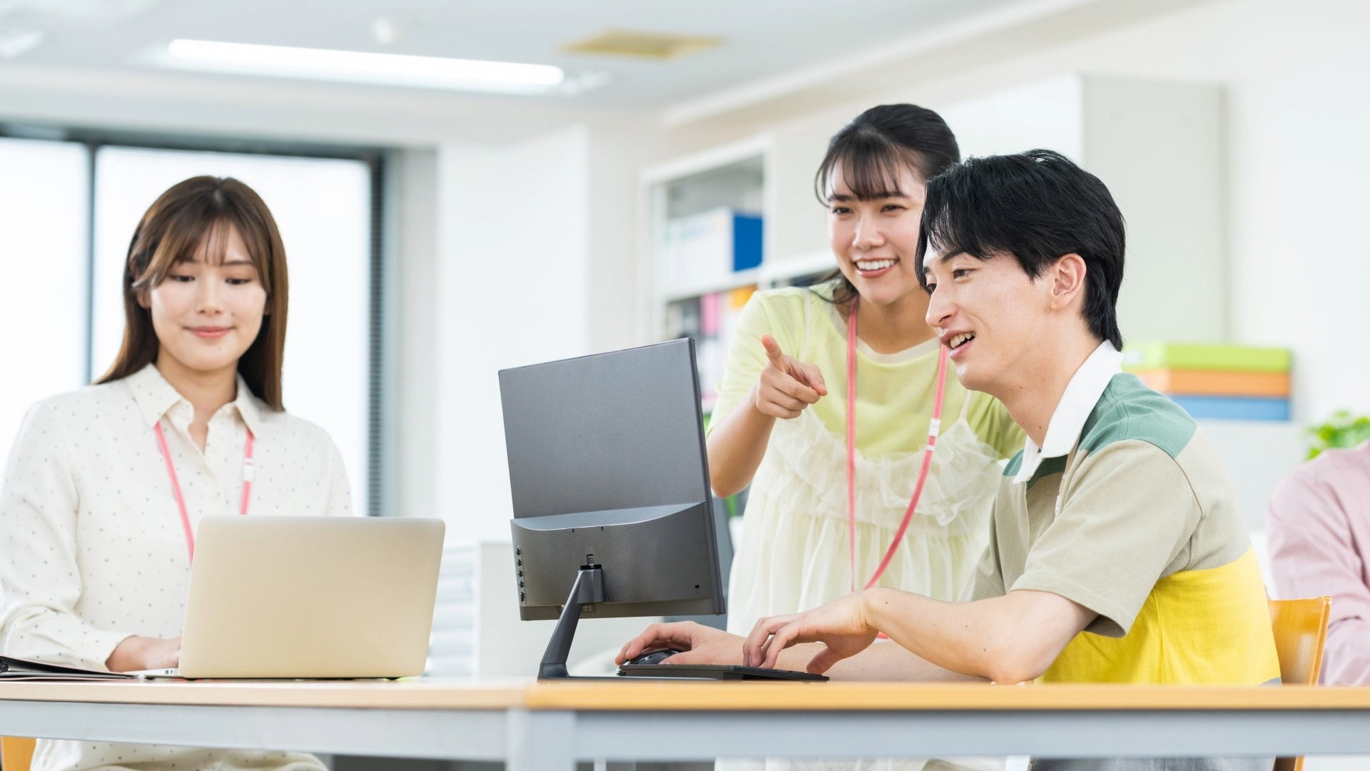 チームメンバーとPC画面でKPIの推移を共有し、成功させるポイントについてアドバイスを受ける若手社員。