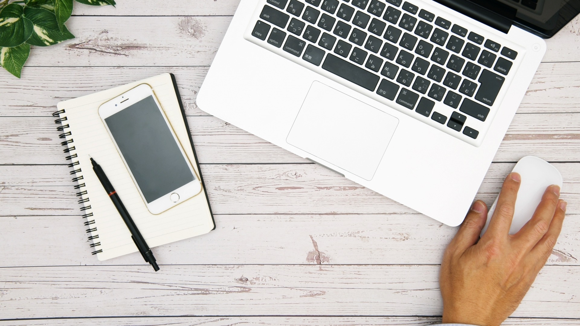 オウンドメディアのKPI設定ガイドを執筆するライターのデスク環境。PC、スマートフォン、取材メモが効率的に並ぶ。