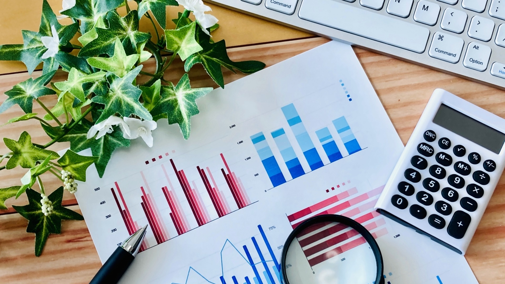 オウンドメディアの目的別指標を可視化した棒グラフや円グラフの資料と、分析に使用する電卓や拡大鏡。