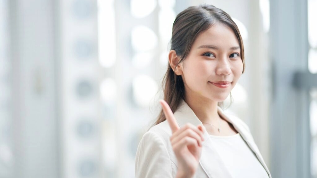 人差し指を見せるオウンドメディア担当の女性社員。他社との差別化を図るための方法について説明しているイメージ。